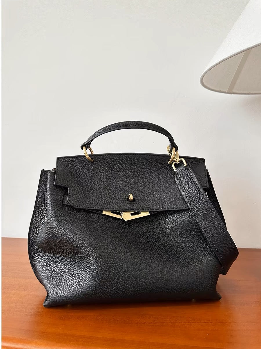 Black leather satchel bag with removable crossbody strap on a table